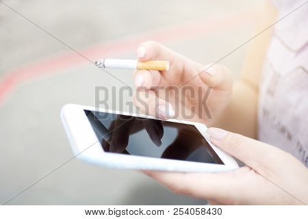 Woman Hand Holding Smoking Cigarette And Using Mobile Smart Phone With Black Blank Screen