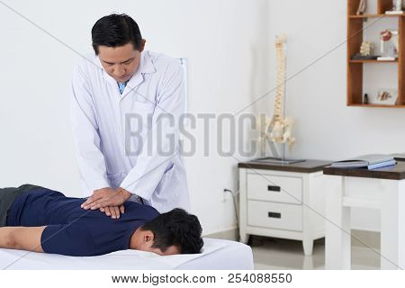 Professional Vietnamese Chiropractor Doing Pushing Motion To Adjust Spine Of Male Patient
