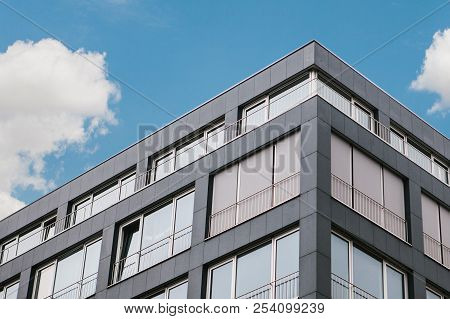 The Corner Of The Building With Many Windows In A Minimalistic Style Against The Blue Sky.