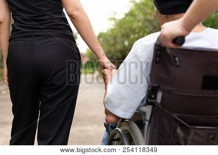 Caretaker And Daughter Spending Time Outdoor With Patient In Wheelchair.