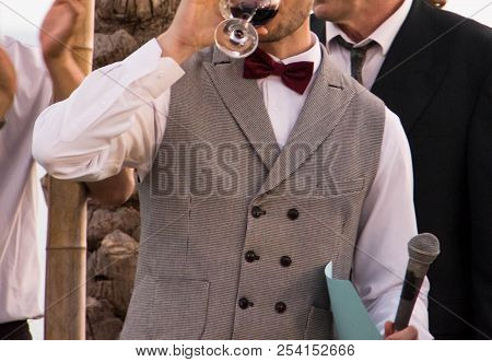 The Happy Groom In A Fashionable Suit Drinks Red Wine From A Glass