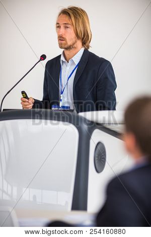 Handsome young man giving a speech at a conference - elegant and outspoken millennial presenting his business venture to investors/scientist talking about his research