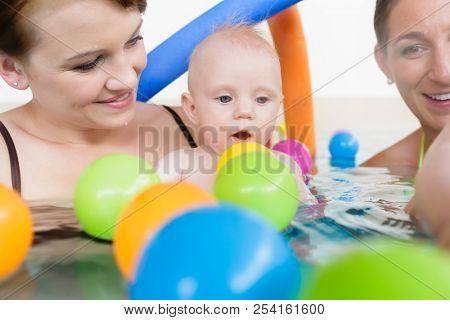 Mothers and their kids having fun at baby swimming lesson between lots of water balls