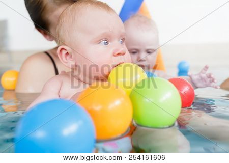 Mothers and their kids having fun at baby swimming lesson between lots of water balls