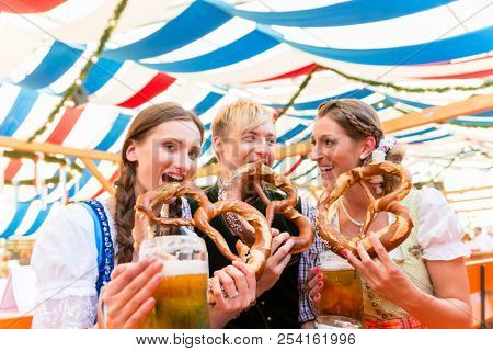 Three friends at the Regensburger Dult eat giant pretzels and drink beer in tent 