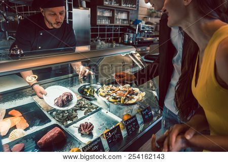 Experienced chef choosing raw seafood from the freezer for two customers in a trendy restaurant or cafeteria with fresh food