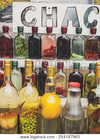Traditional Georgian Alcohol Drink Chacha In Bottles With Different Fruits And Herbs At Market