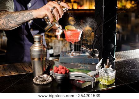 Barman Spraying Peat Bitter On A Glass With Red Sweet Summer Cocktail Arranged On Books On The Bar C