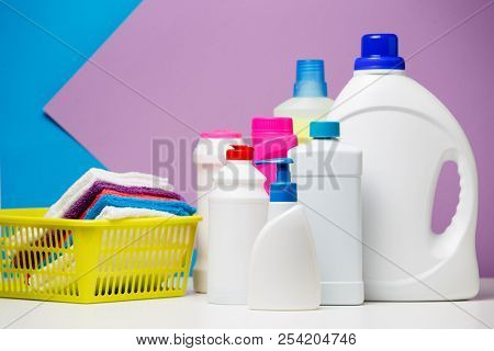 Photo of several bottles of detergents and multi-colored towels in basket isolated on purple, blue background