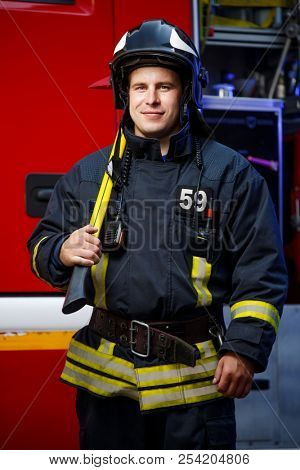 Photo of fireman wearing helmet with hammer against fire engine