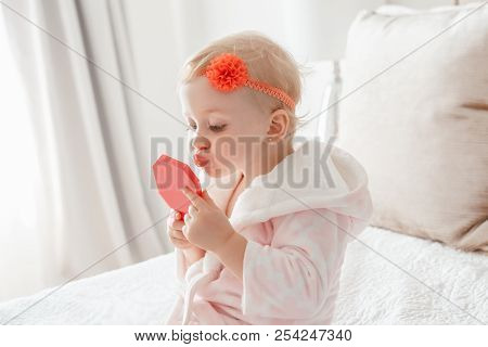 Cute Asorable Funny Caucasian Blonde Baby Girl 2 Years Old In Bathrobe Looking Into Mirror. Toddler 