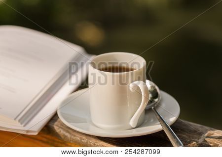 Cup Of Hot Coffee For Brackfast And Book On Wooden Balcony Near River And Mountain Background