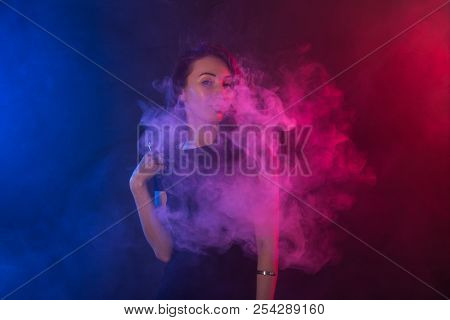 Young Woman In Neon Light And Smoke Of E-cigarettes Or Vape On Dark Background