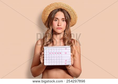 Horizontal Shot Of Displeased Young European Female Tourist In Summer Straw Hat Holds Period Calenda