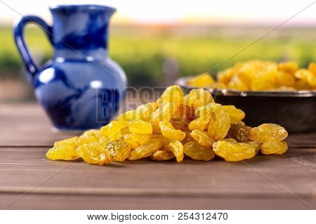 Lot Of Whole Dry Golden Raisins Sultana Variety With Blue Jar With Vineyard In Background