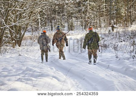 Group Of Hunters In Winter Forest With Carbines And Shotgun