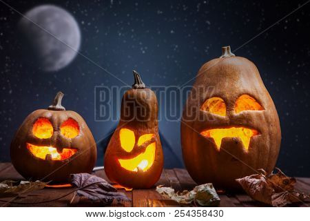 Jack o lanterns Halloween pumpkin face on wooden background and autumn leafs