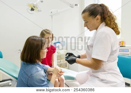 Mother And Little Daughter Visiting Dentist At Dental Clinics. Orthodontist Puts On, Corrects The De