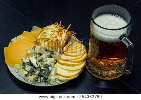 A Glass Of Light Beer Ipa And A Plate Of Sliced ​​cheese Of Different Varieties On A Dark Table