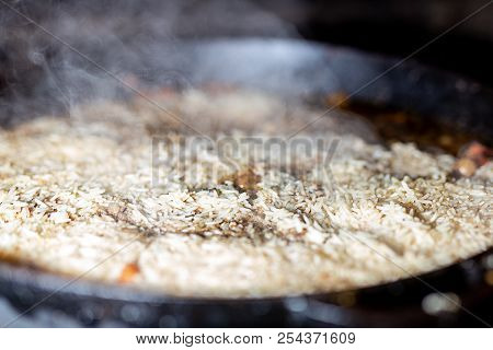 Cooking Rice For Pilaw Or Paella In Iron Cauldron Over Open Fire. Smoke And Steam. Tasty Food Prepar
