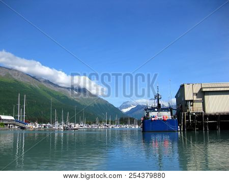 Blue Fishing Boat Is Docked Alongside A Wharf In The Port Of Valdez, Alaska.  Small Boat Harbor Can 