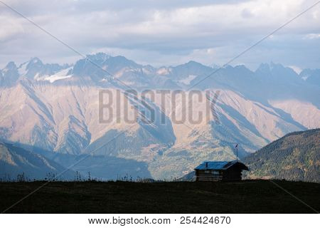 Mountain landscape. Peak in clouds. Beautiful sunset. Wooden house of shepherds on a hillside Mkheer. Caucasus, Zemo Svaneti, Georgia 