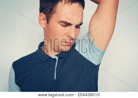 A Young Guy In A Polo Shirt Sniffs His Smelly Armpit And Makes A Disgruntled Expression On Blue Back