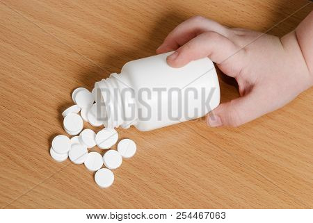 Child's Hand Touching A Bottle Of Pills.