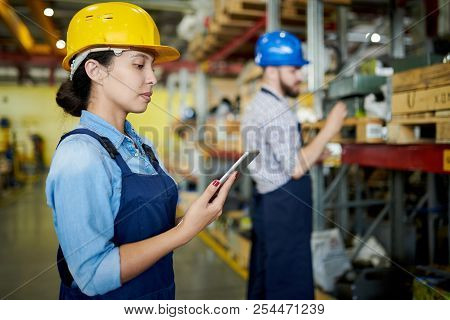 Side View Portrait Of Female Factory Worker Wearing Hardhat Using Digital Tablet In Workshop With An