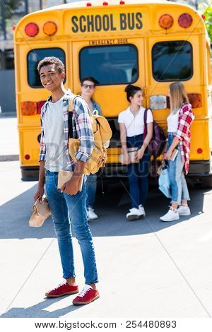 Handsome Smiling Teen Schoolboy Looking At Camera While His Classmates Standing Behind Near School B