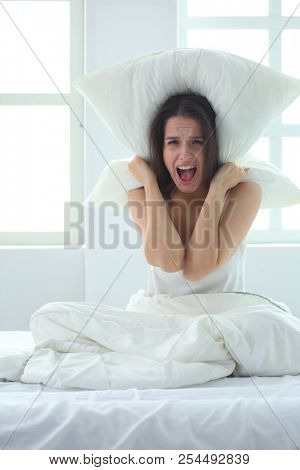 Young caucasian woman covering her head and ears with pillows.