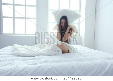 Young caucasian woman covering her head and ears with pillows.