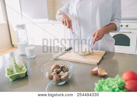Cut View Of Girl In White Shirt Stands At Table And Blending Together Milk With Eggs. She Holds Glas