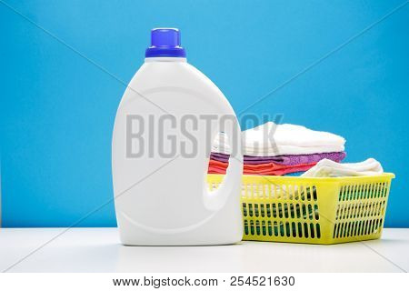 Photo of one bottle of detergents and yellow basket with towels on empty blue background