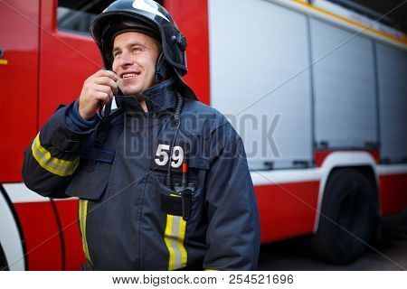 Photo of smiling fireman talking on walkie-talkie with fire engine
