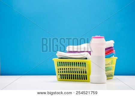 Photo of one bottle of cleaning powder and multi-colored towels in basket isolated on blue background
