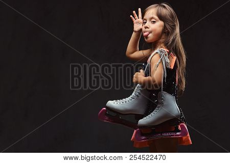 Playful Little Girl Dressed In Skater Dress Holds Ice Skates Makes Faces And The Pulled Out Tongue. 