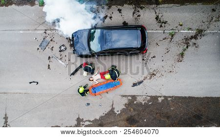 Three Firefighters Helping A Young Injured Woman Lying On The Road After An Accident.