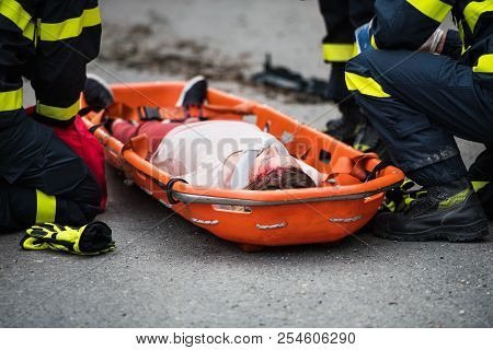Firefighters Putting An Injured Woman Into A Plastic Stretcher After A Car Accident.