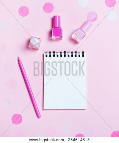 Empty Note Pad And Colorful Nail Polishes On Pink Confetti Background.