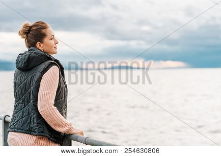 Outdoor Portrait Of Young Woman Resting By The Lake On A Fresh Cold Day, Wearing Warm Pullover