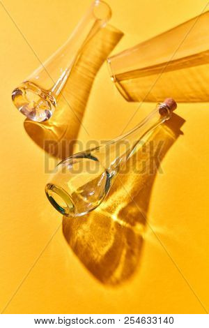 Empty glass bottles lie on a yellow background with shadows and reflection, copy space. Top view. Various glass chemistry lab equipment. Science and medical background.