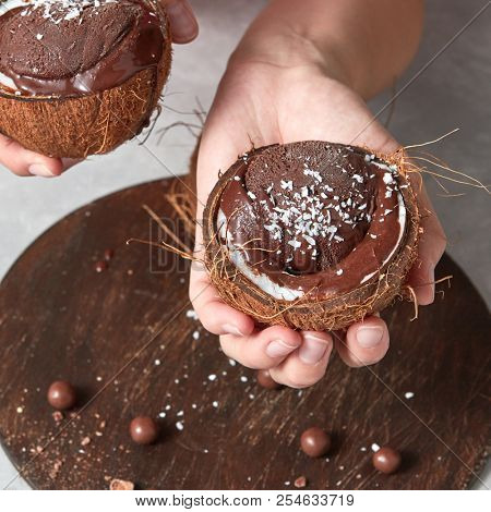 Delicious melted cocolate dessert, ice cream in a coconut shell in a girls hands above a wooden board on a gray background. Vegetarian concept of diet eating
