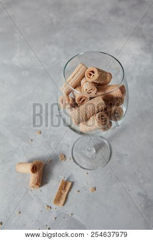 A glass with delicious wafer cripsy rolls on a gray concrete table and place for text.