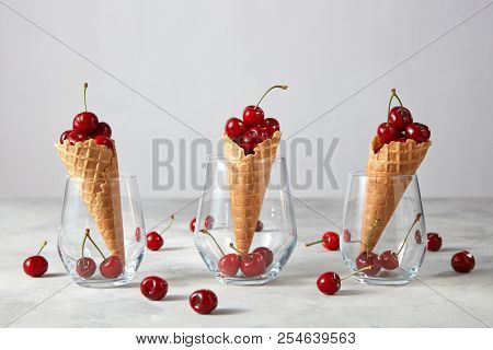 The glass cups with crispy waffle cones and ripe red cherries on a gray srone table, background , copy space. Summer concept of homemade cake.