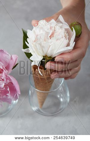 Cripsy waffle cup of a delicate white pion in a glass cup with gerls hand on a gray marble table.