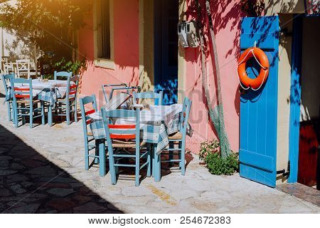 Traditional Greek Vivid Lilac Colored Tavern On The Narrow Mediterranean Street On Hot Summer Day