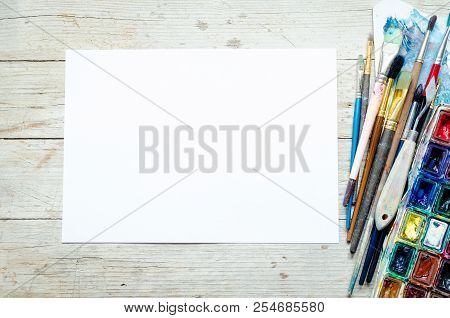 Artist Paint Brushes And Watercolor Paintbox On Wooden Background With Empty Sheet Of Paper. Instrum