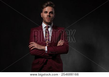 portrait of confident man wearing a red suit standing on grey background with arms crossed