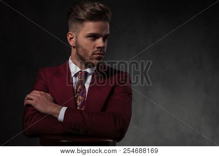 stylish man relaxing at wooden bar table looks to side while standing on grey wallpaper background, portrait picture